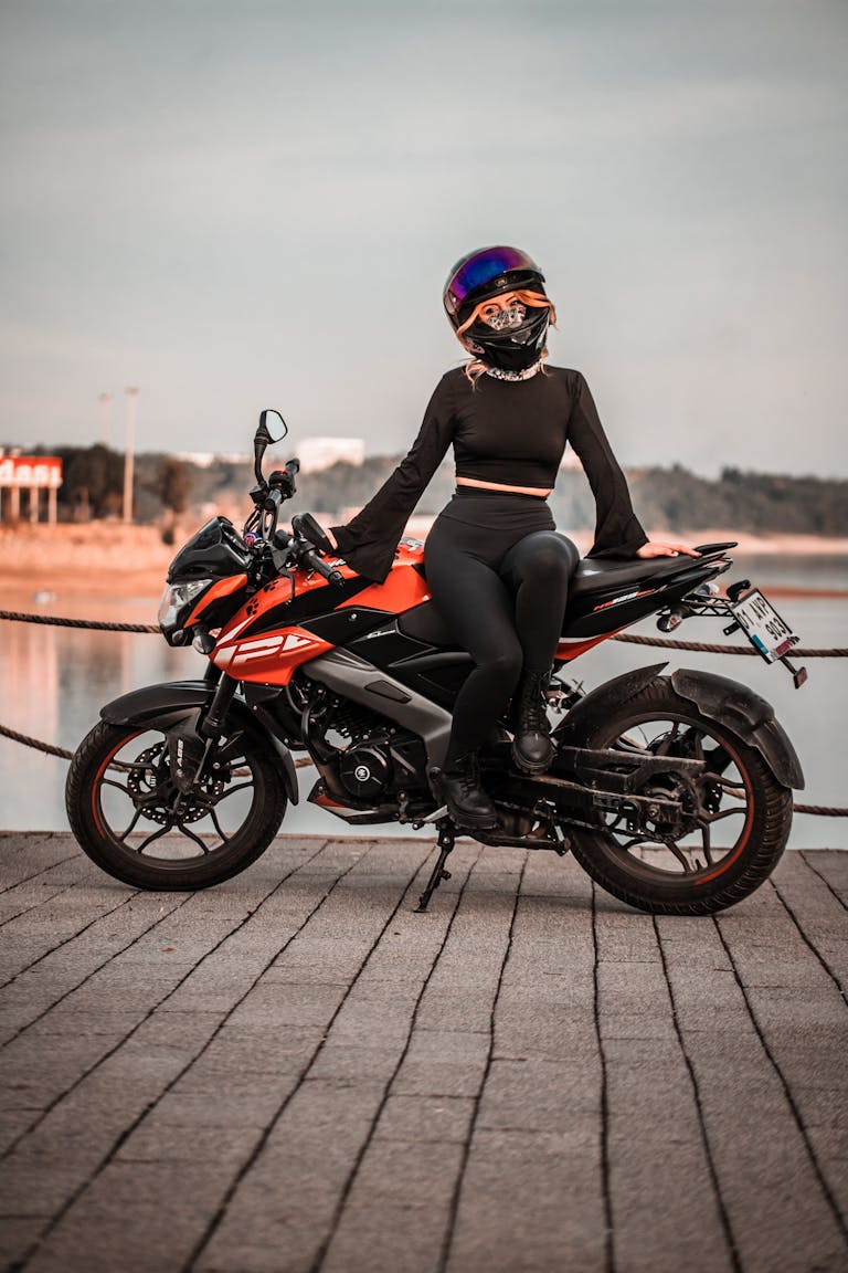 A woman in full gear on a motorcycle by a lakeside at sunset.