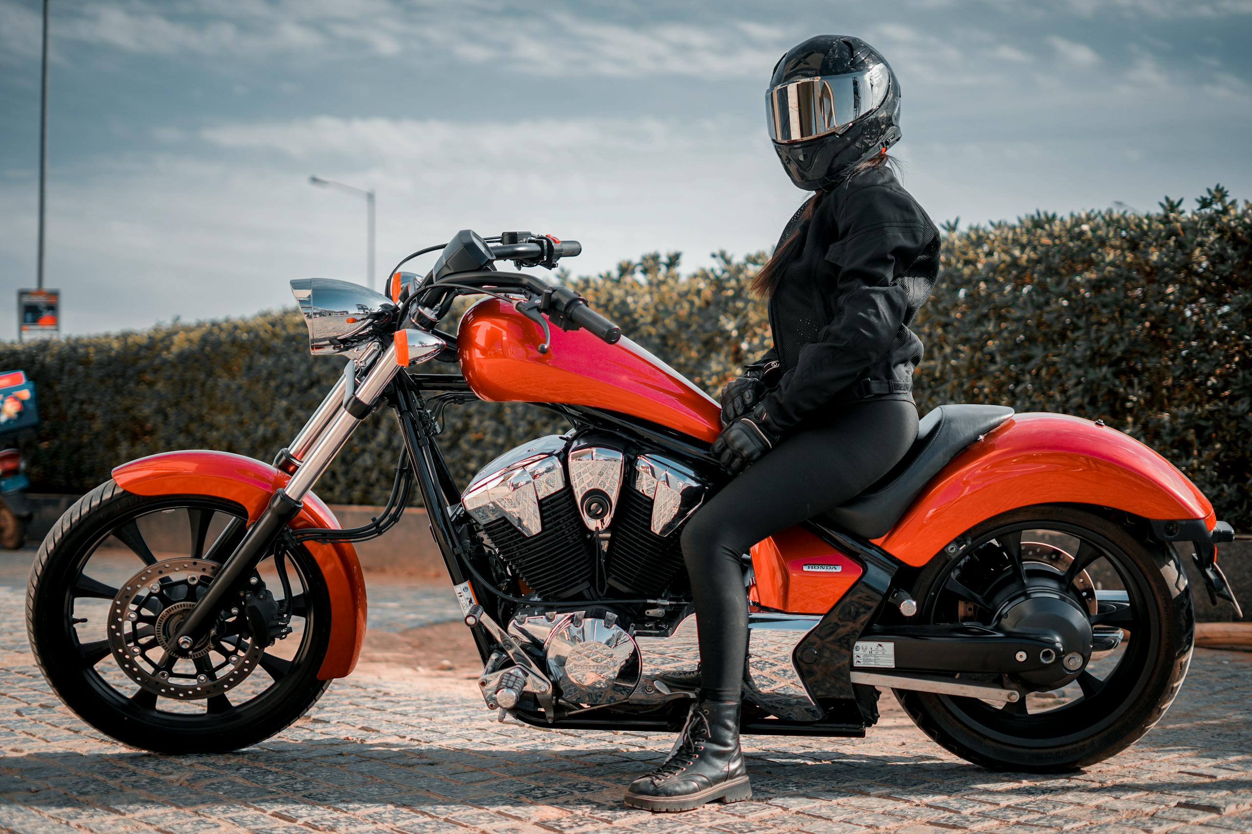 Petite women rider dressed in black motorcycle jacket on a red chopper motorcycle in California, outdoors.